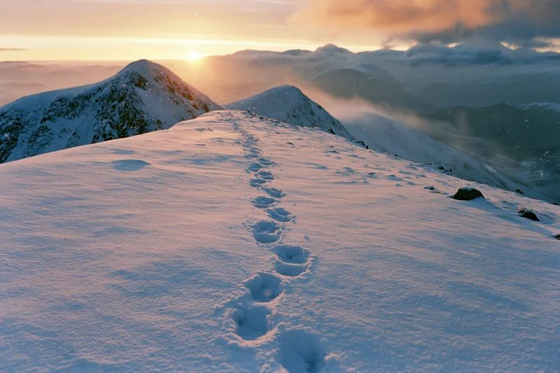 Footprints leading across a snow-covered mountain ridge at sunrise