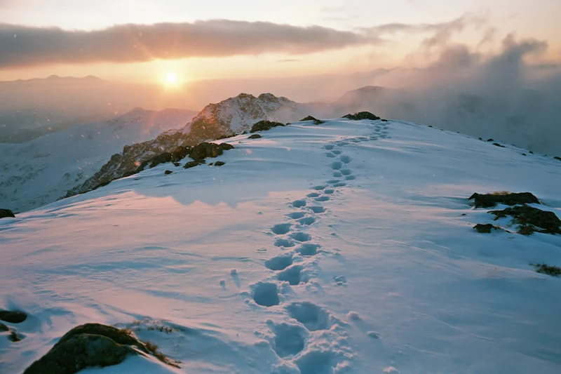 Footprints trailing across a snow-covered mountain ridge at sunset