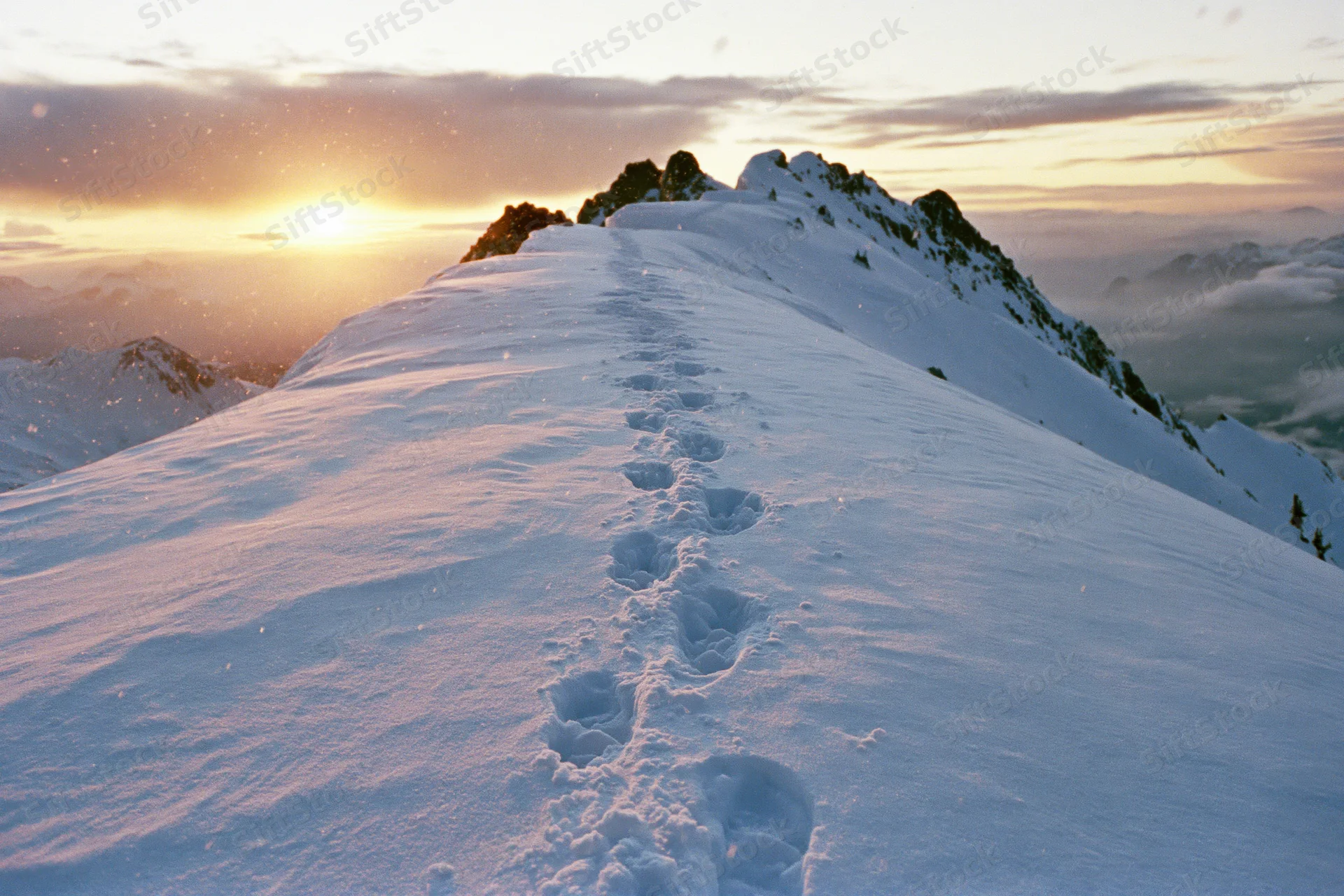 Footprints leading across snow-covered mountain ridge at sunset