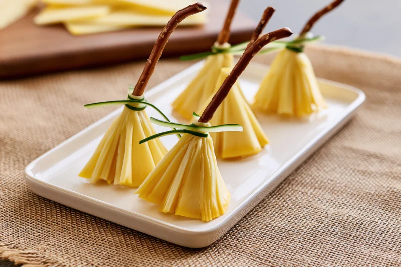 Cheese witch broom appetizers arranged on a white ceramic tray on burlap fabric