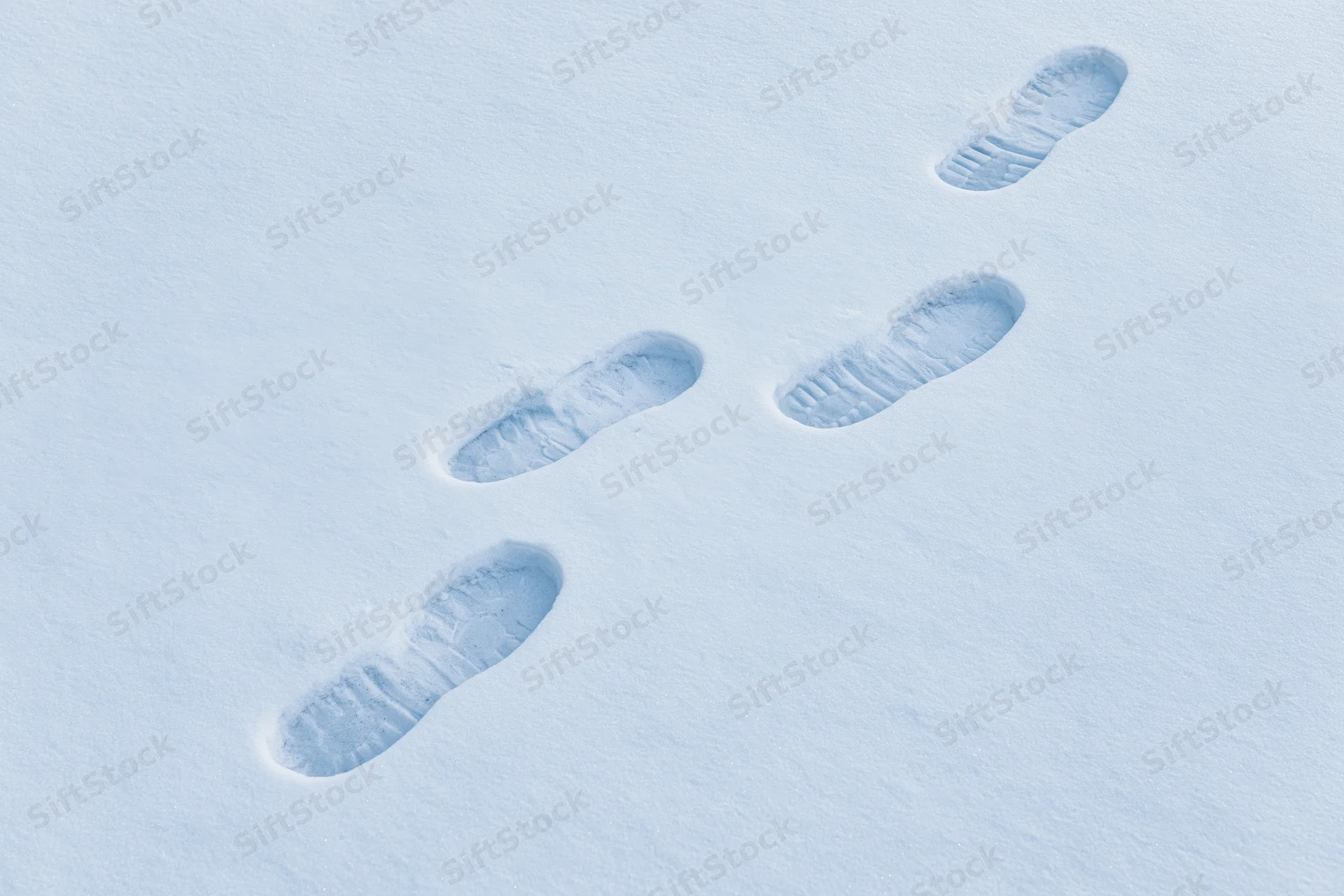 Four human footprints in fresh snow forming a path across a snowy field