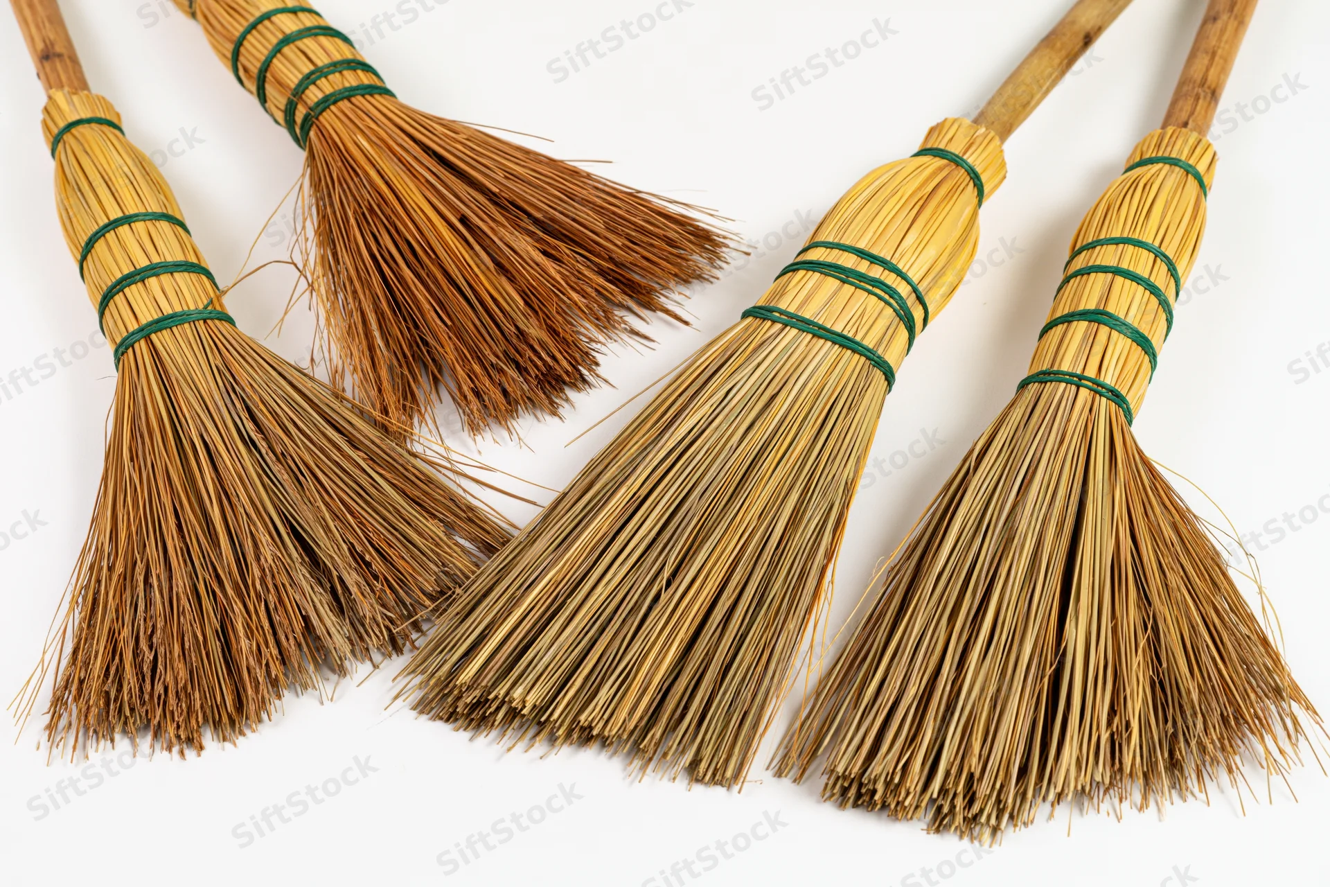 Four traditional straw hand brooms arranged in a flat lay on white background