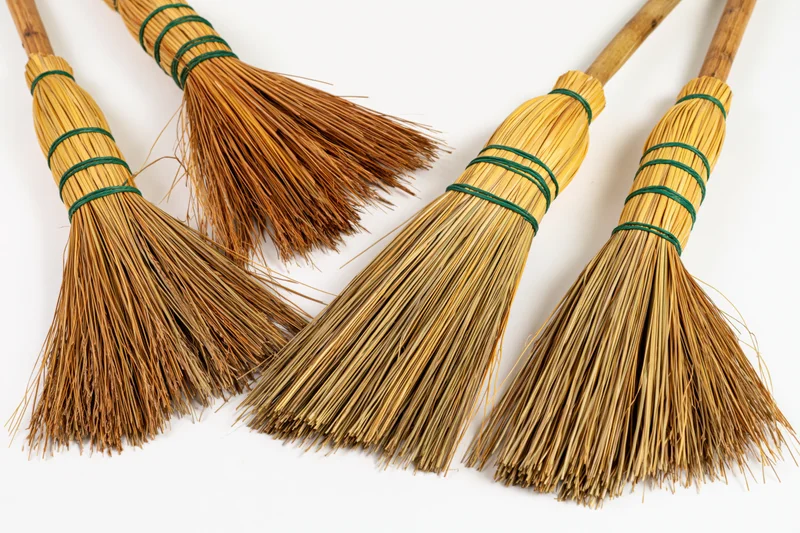 Four traditional straw hand brooms arranged in a flat lay on white background
