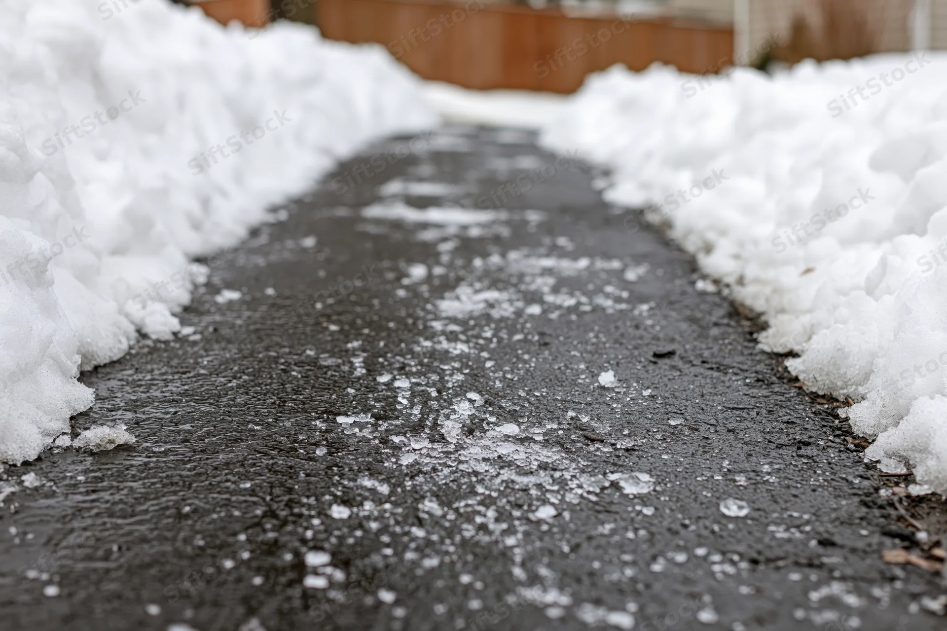 Cleared asphalt driveway with snowbanks on sides and icy patches in winter