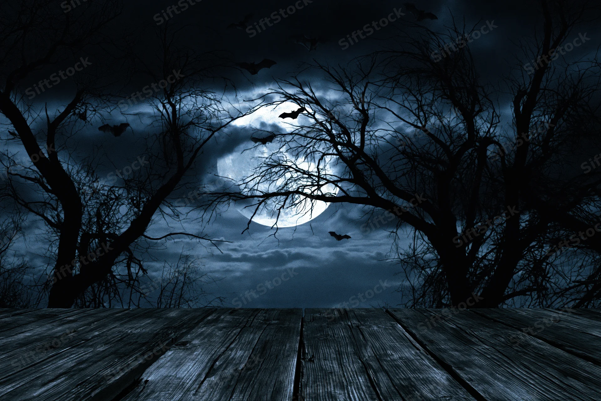 Full moon glowing behind silhouetted bare tree branches with bats flying over a wooden deck at night