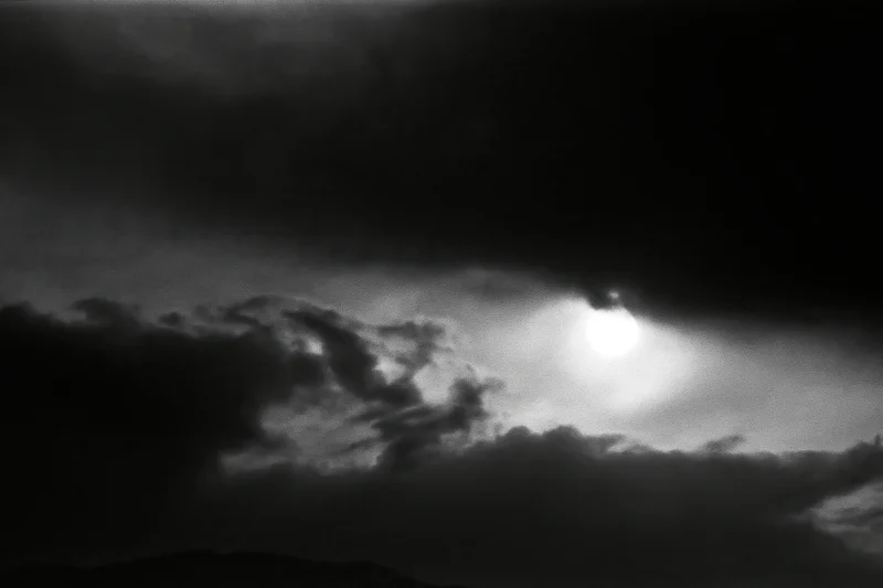 Full moon partially hidden by dark storm clouds in a monochrome night sky