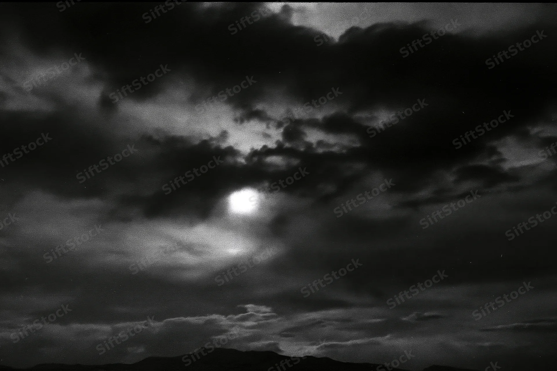 Full moon glowing through dark storm clouds above mountain silhouette at night