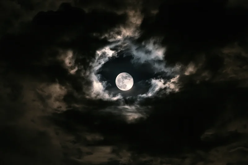 Full moon glowing through a break in dense clouds at night