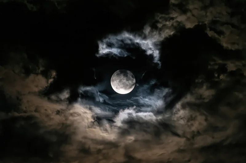 Full moon glowing through a break in dense clouds at night