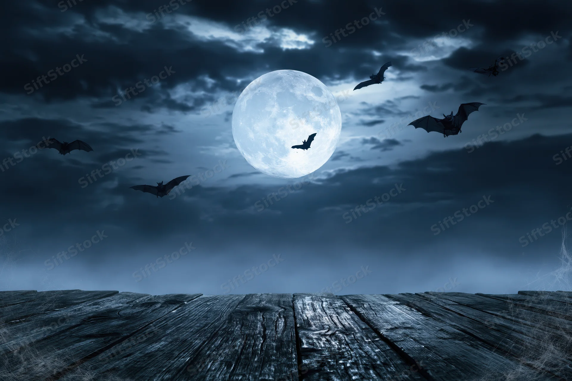 Full moon rising over misty night sky with silhouetted bats flying above wooden deck