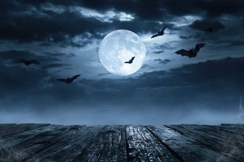 Full moon rising over misty night sky with silhouetted bats flying above wooden deck