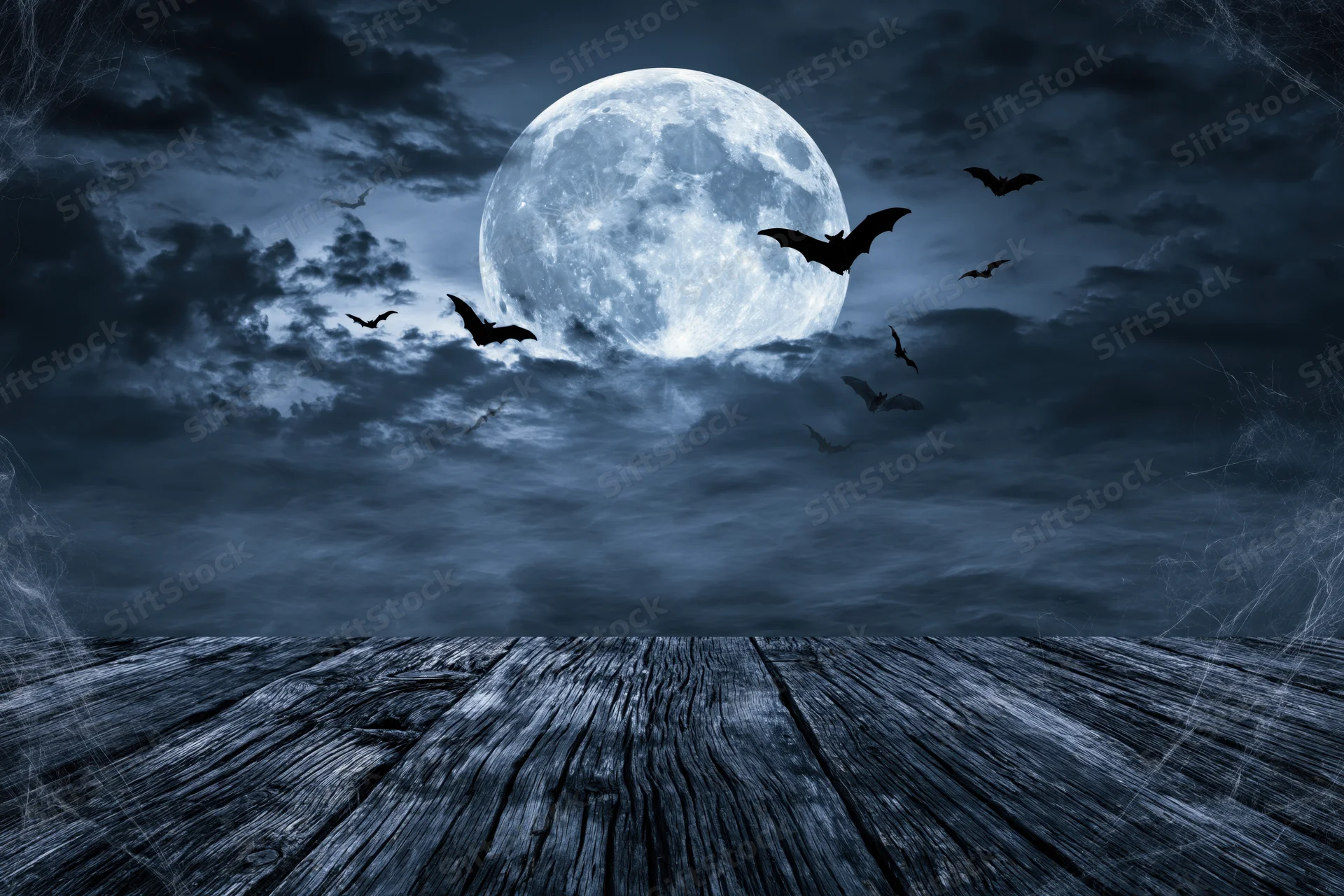 Full moon rising over misty night sky with silhouetted bats above wooden deck