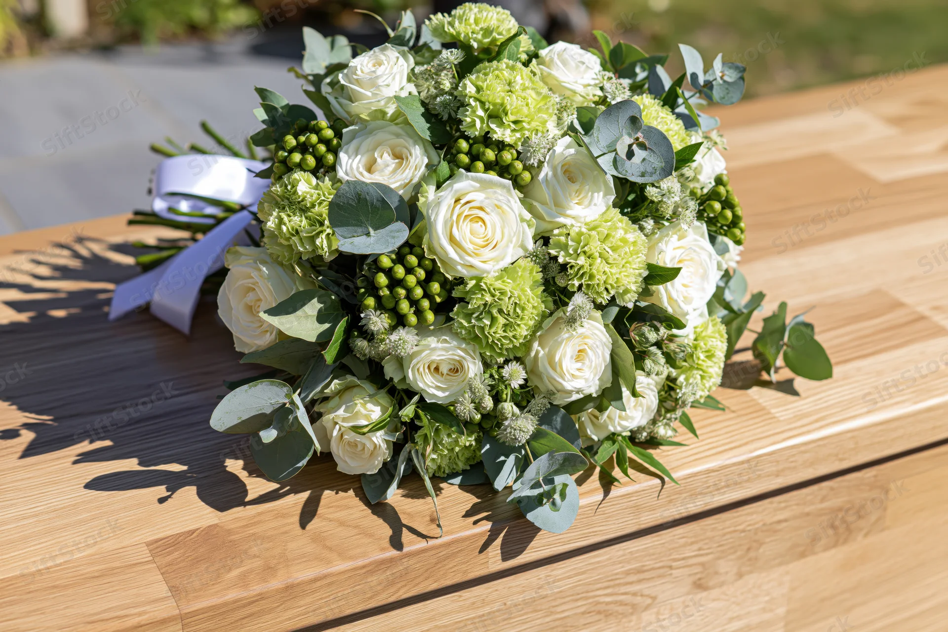 Floral arrangement with white roses and green hydrangeas resting on wooden coffin