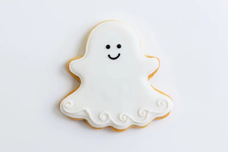 Ghost-shaped sugar cookie with white icing and smiling face on white background