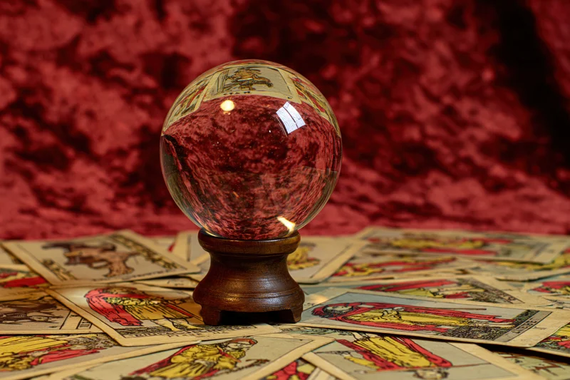Crystal ball on wooden stand surrounded by scattered tarot cards on red velvet background