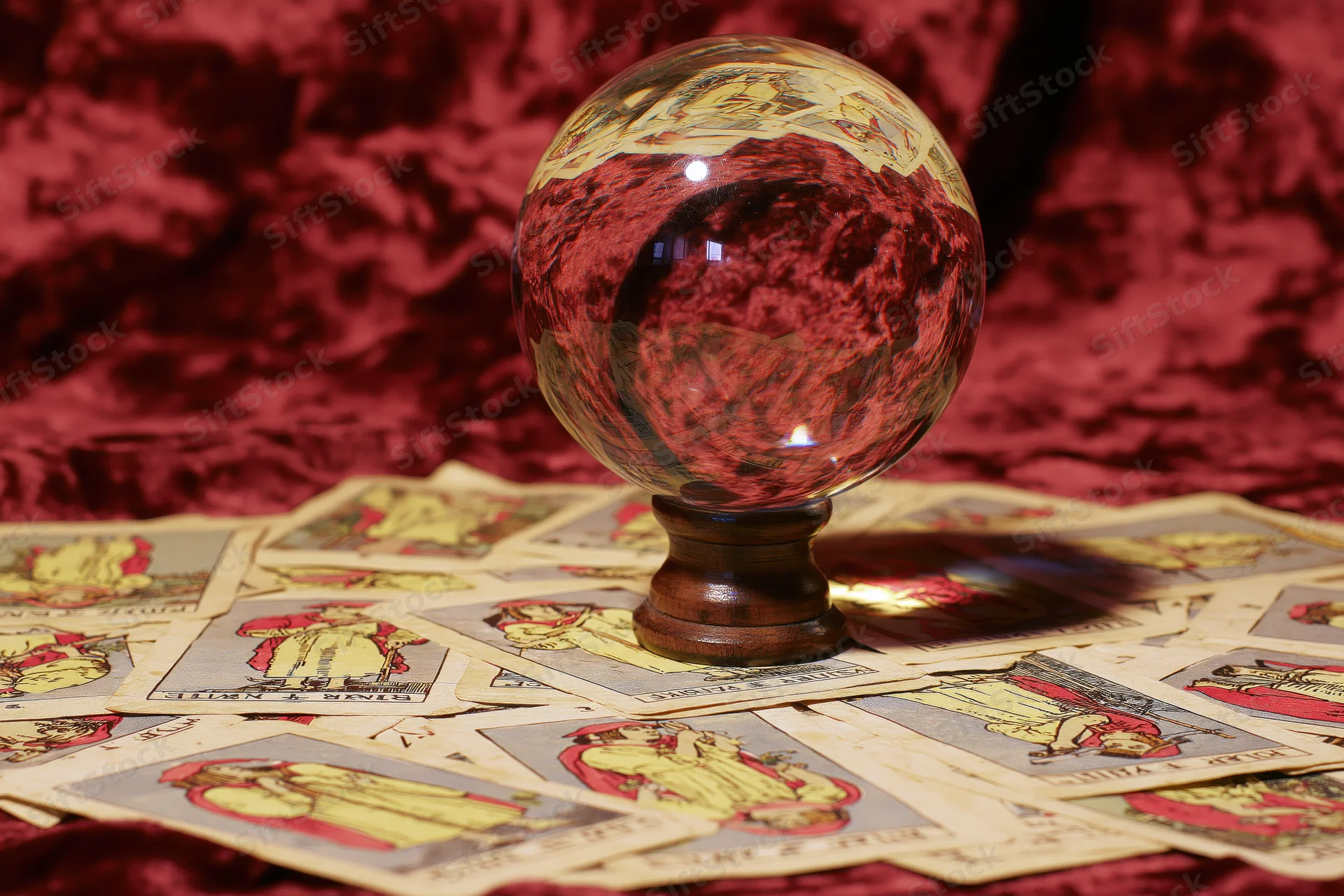 Crystal ball on wooden stand surrounded by scattered tarot cards on red velvet surface