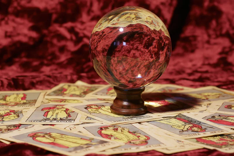 Crystal ball on wooden stand surrounded by scattered tarot cards on red velvet surface