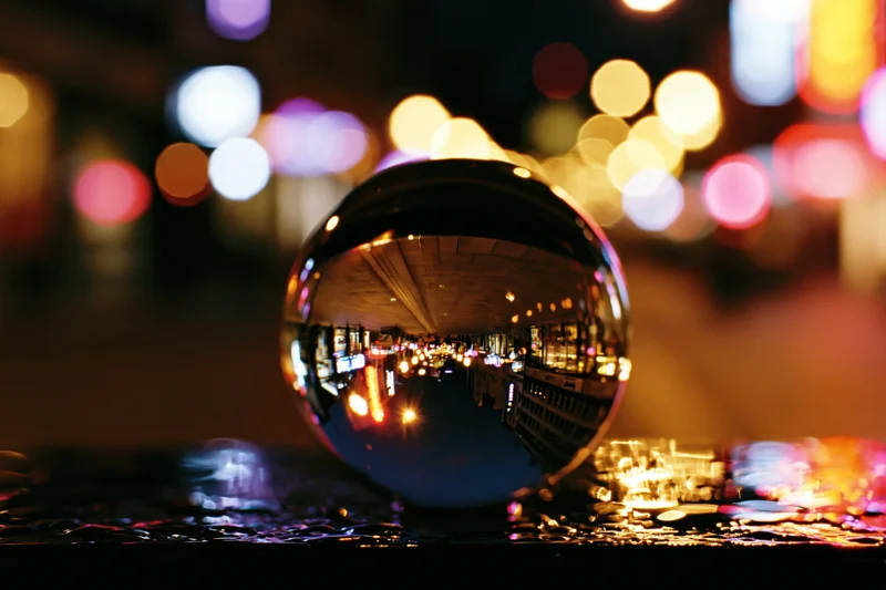 Crystal ball reflecting inverted city lights at night on wet pavement