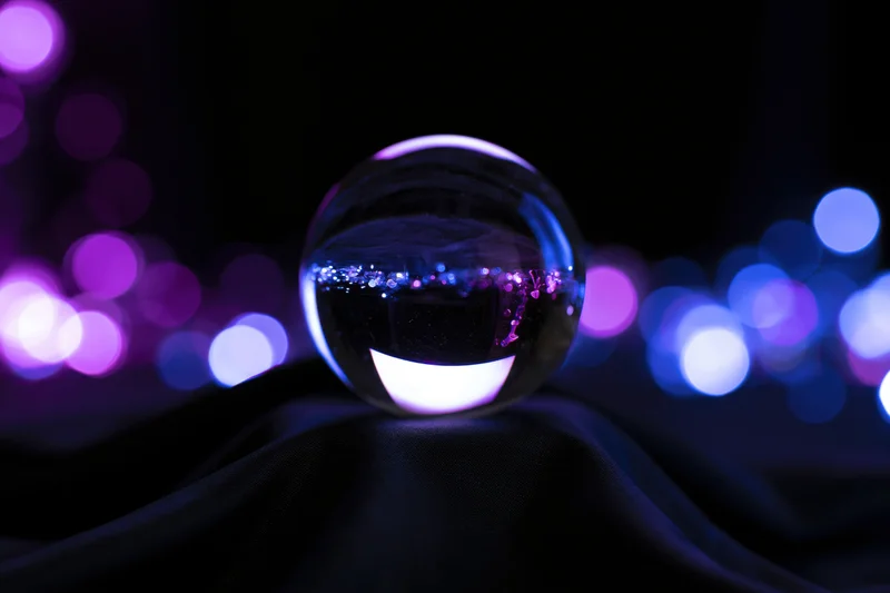 Glass crystal ball resting on dark draped fabric with purple and blue bokeh lights in background