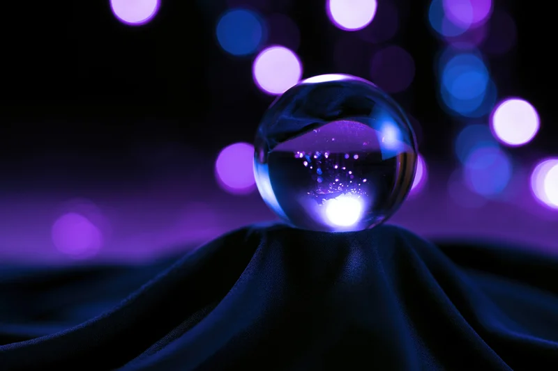 Glass crystal ball resting on dark draped fabric with purple and blue bokeh lights in background