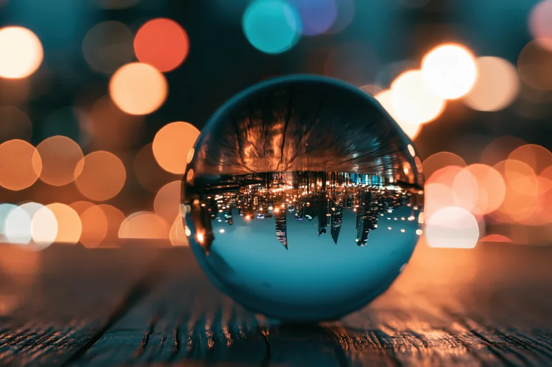 Glass lensball reflecting inverted cityscape at night on wooden surface