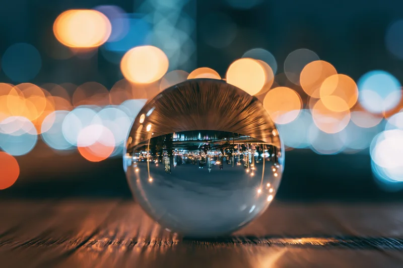 Glass lensball reflecting inverted cityscape at night on wooden surface
