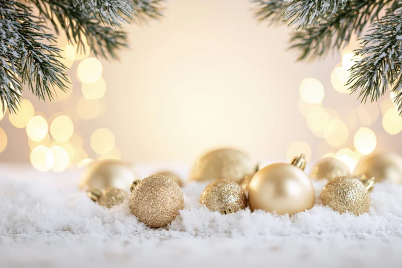 Gold christmas ornaments resting on snow with pine branches and bokeh lights in background
