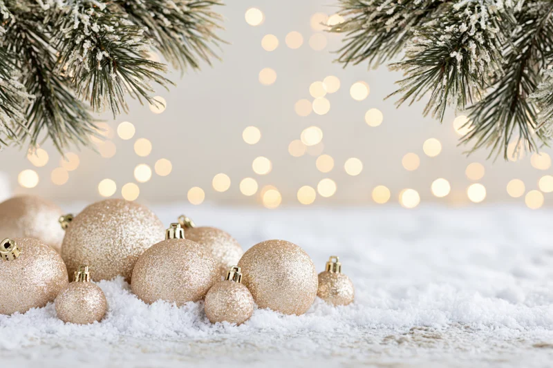 Gold christmas ornaments resting on snow with pine branches and bokeh lights in background