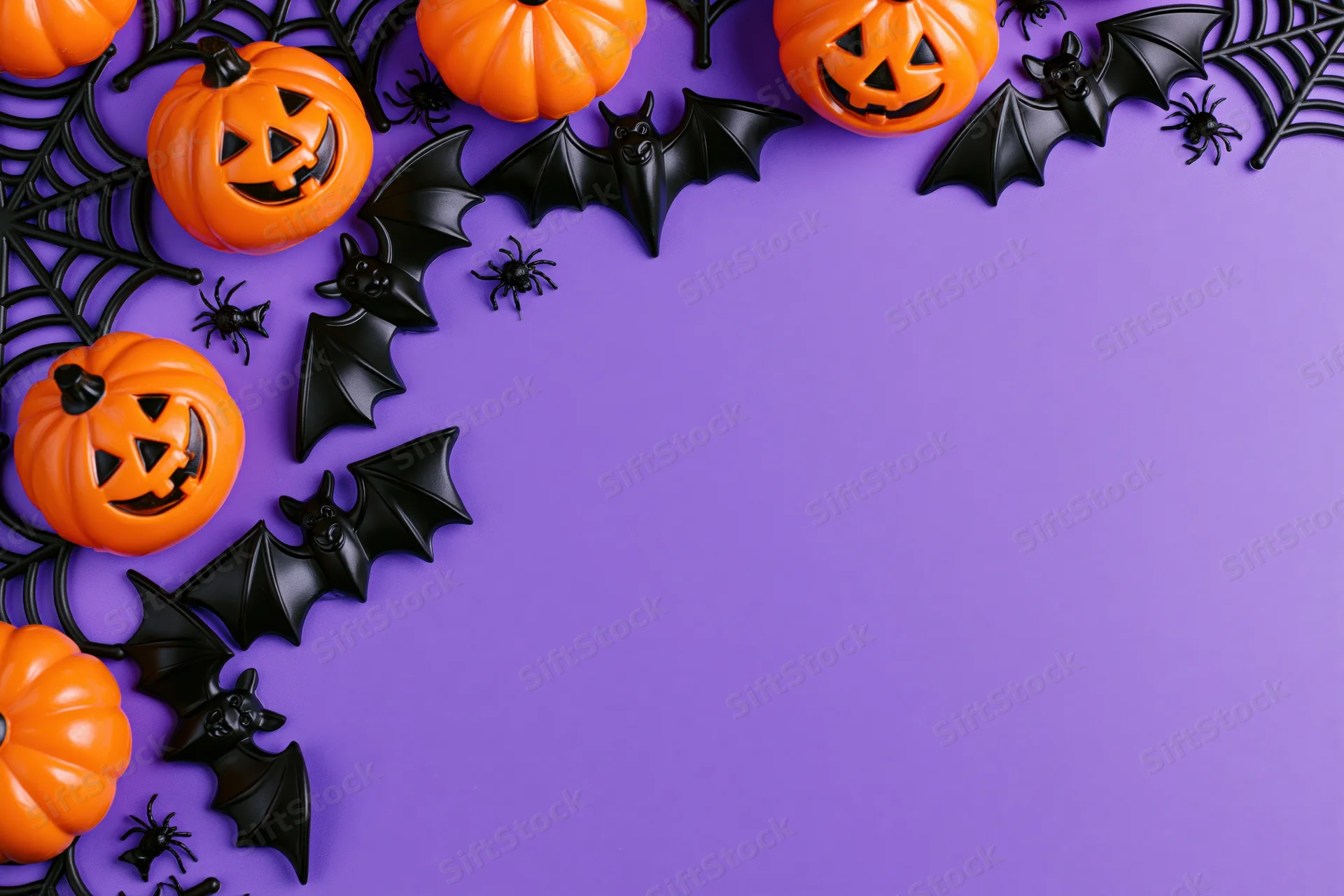 Halloween decorations arranged as a flat lay border along the top and left side of a purple surface with copyspace