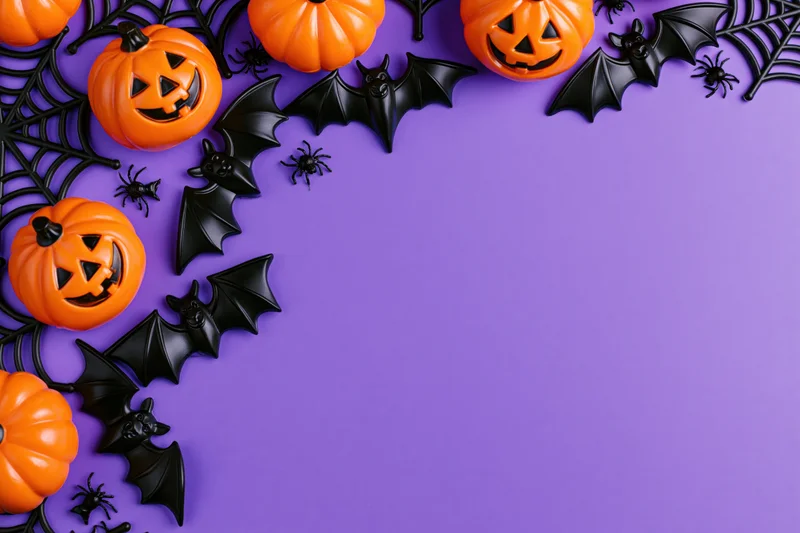 Halloween decorations arranged as a flat lay border along the top and left side of a purple surface with copyspace