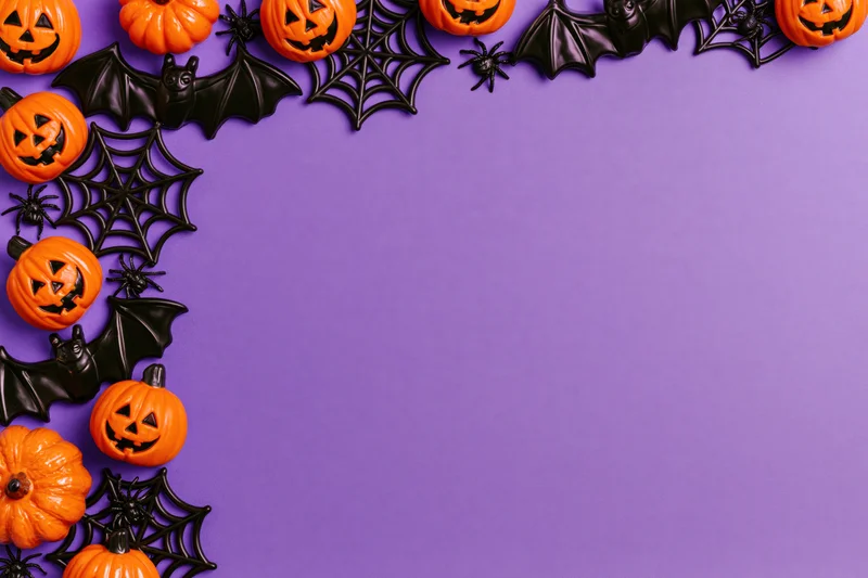 Halloween decorations arranged as a flat lay border along the top and left edge on purple background with copyspace