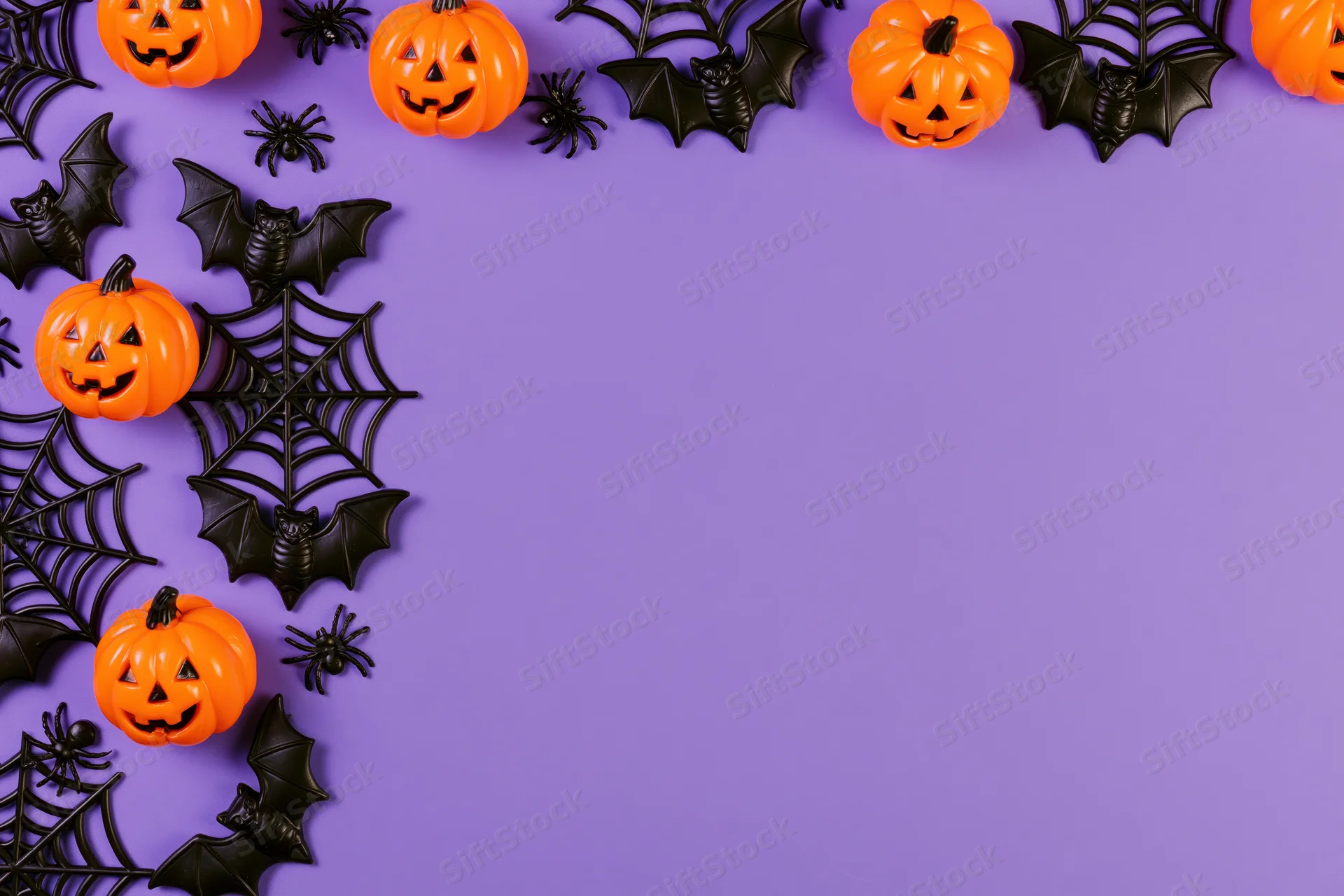 Halloween decorations arranged as a flat lay border along the top and sides of a purple surface with copyspace in the center