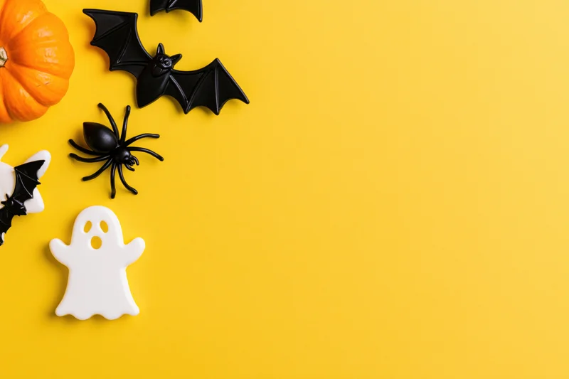 Halloween decorations arranged in flat lay on bright yellow background with copyspace