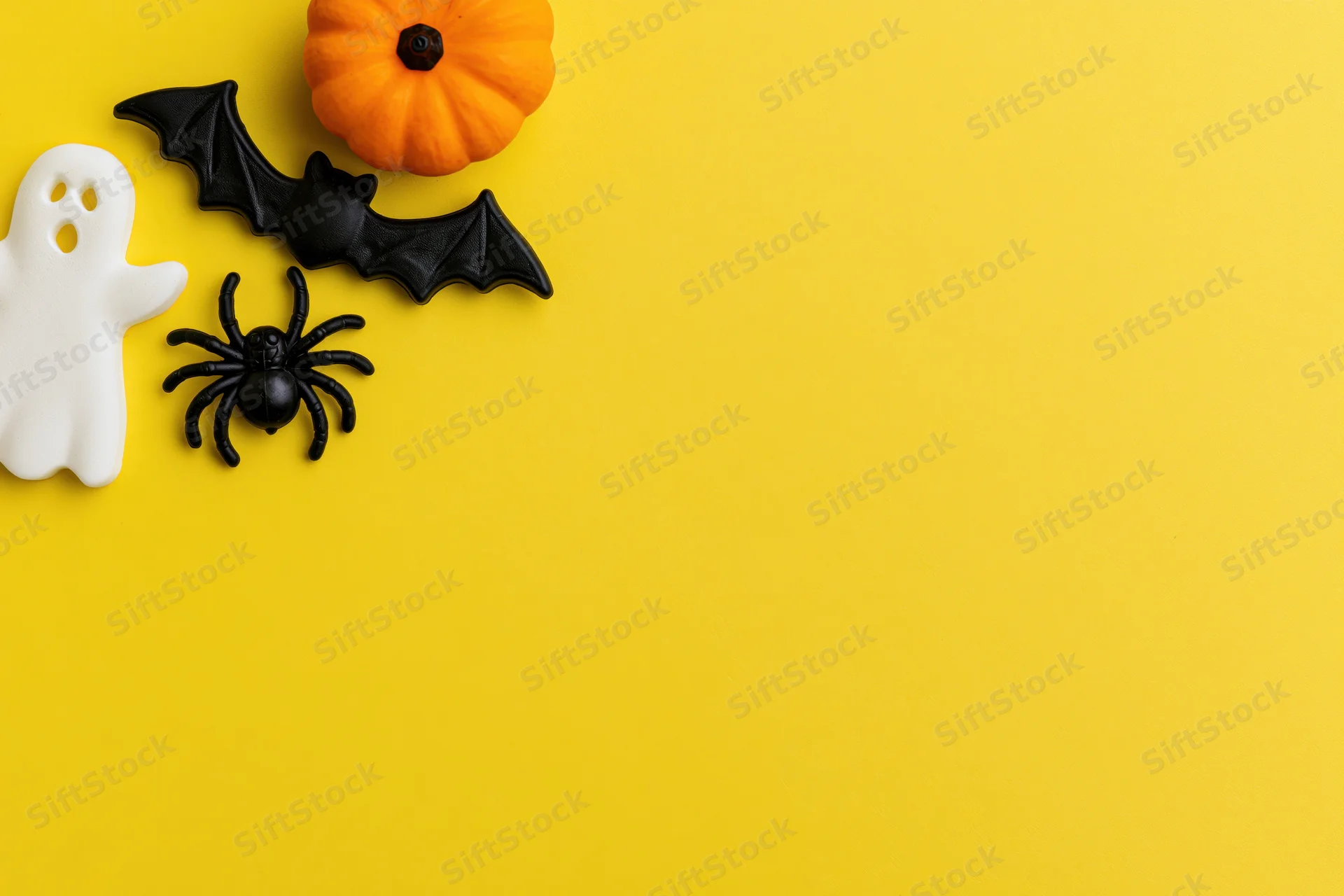 Halloween decorations arranged in flat lay on bright yellow background with copyspace