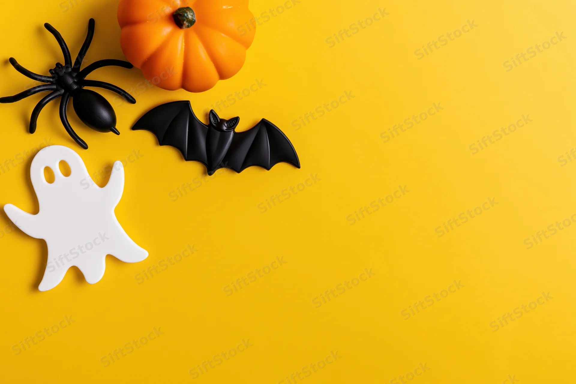 Halloween decorations arranged in flat lay on bright yellow background with copyspace