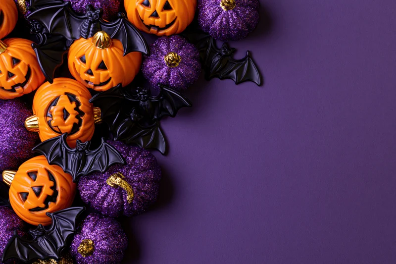 Halloween decorations arranged in corner on purple surface with copyspace