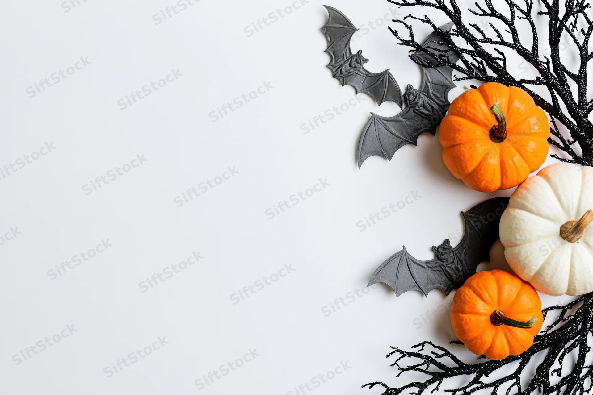 Halloween decorations including pumpkins, bats, and branches arranged along the right edge of a white surface
