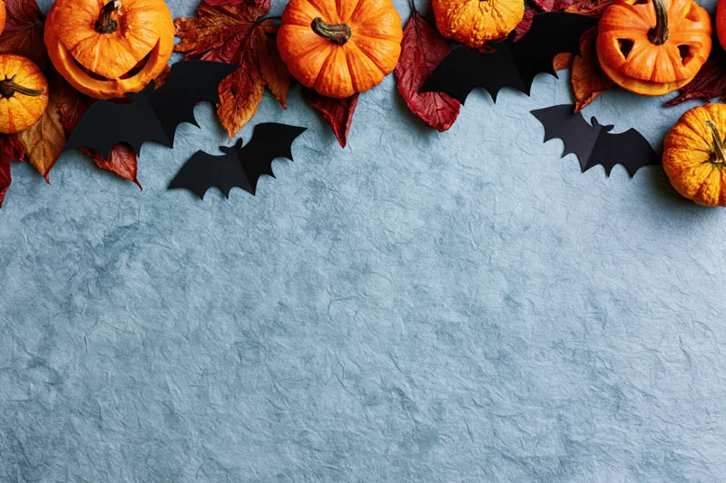 Halloween flat lay with carved pumpkins and paper bats arranged along blue textured surface