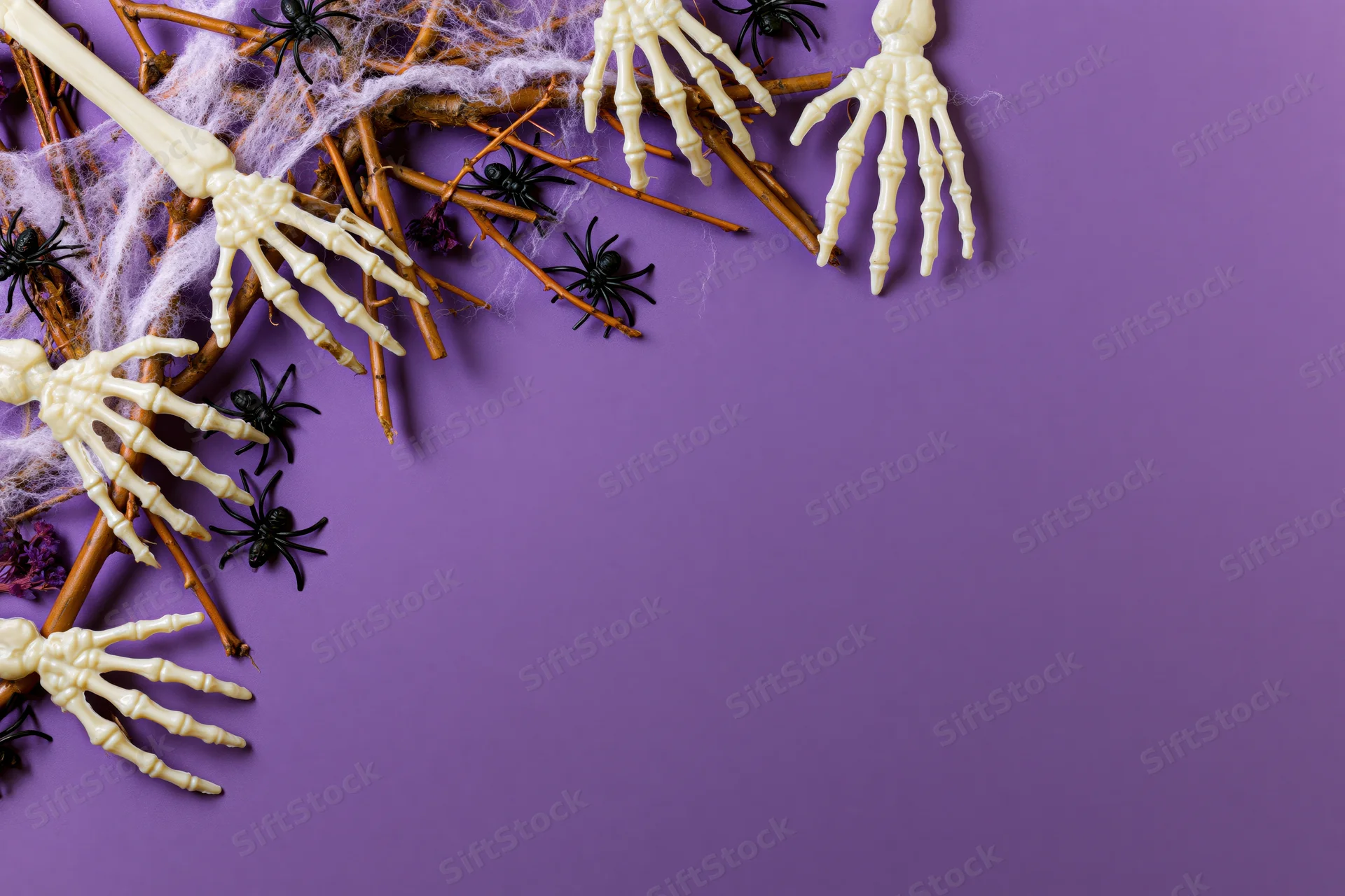 Plastic skeleton hands and spiders arranged with twigs and web on purple surface for halloween decoration