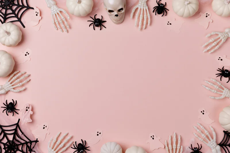 Halloween decorations arranged in a border around a pink surface with copyspace in the center