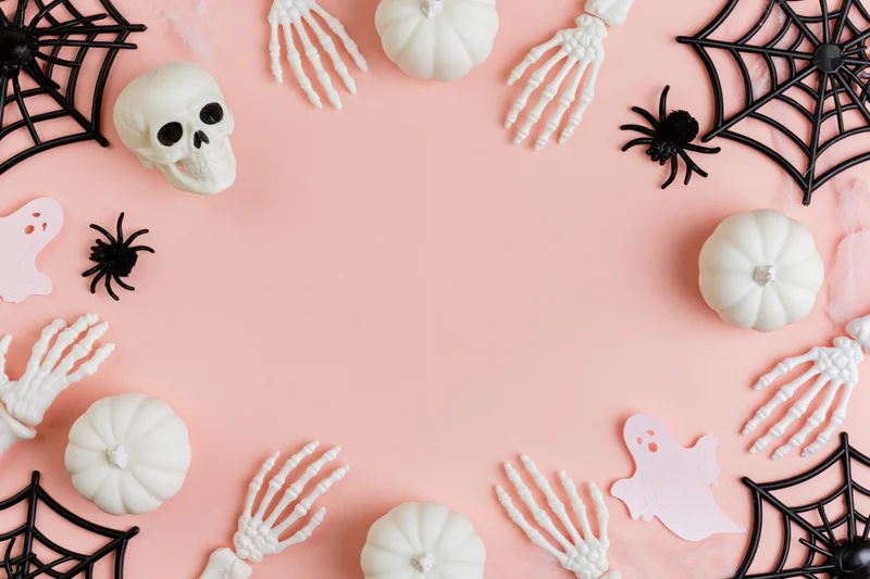 Halloween decorations arranged in a border on a pastel pink surface with copyspace in the center