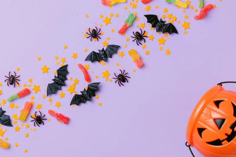 Halloween flat lay with jack o lantern, candy, bats and spiders on purple background