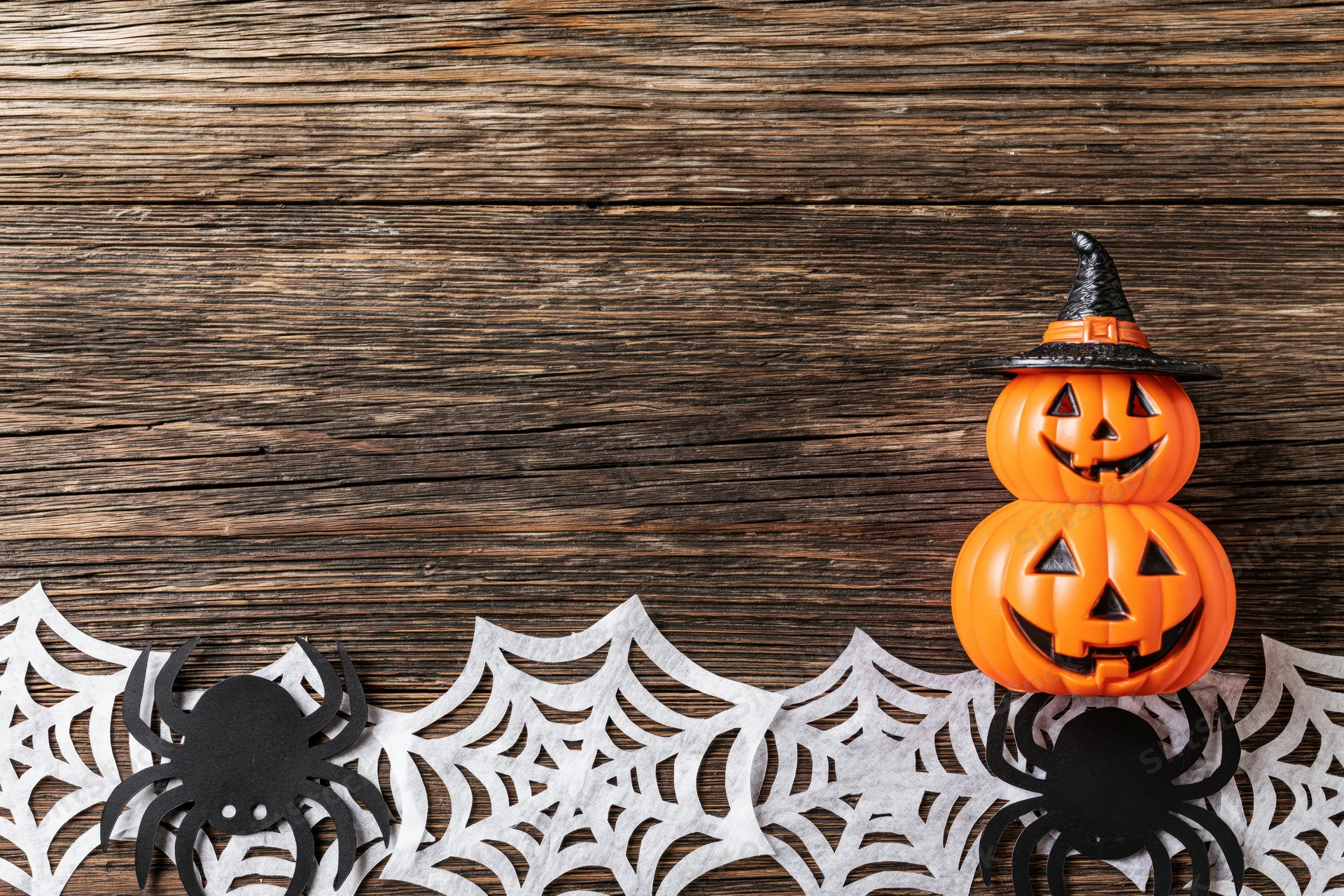 Halloween flat lay with paper spider and web cutouts on wooden surface featuring stacked pumpkins with witch hat and copyspace