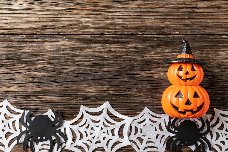 Halloween flat lay with paper spider and web cutouts on wooden surface featuring stacked pumpkins with witch hat and copyspace