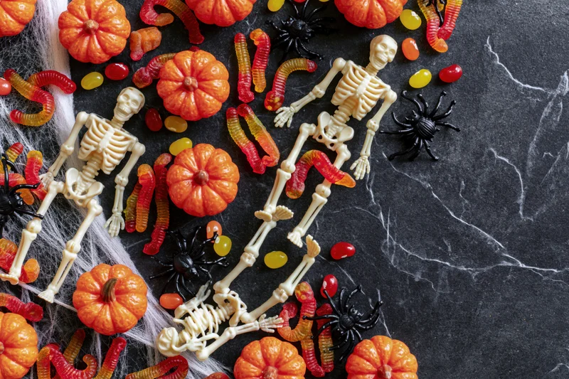 Plastic skeleton figurines and halloween candy arranged on dark marble surface with cobweb and pumpkins