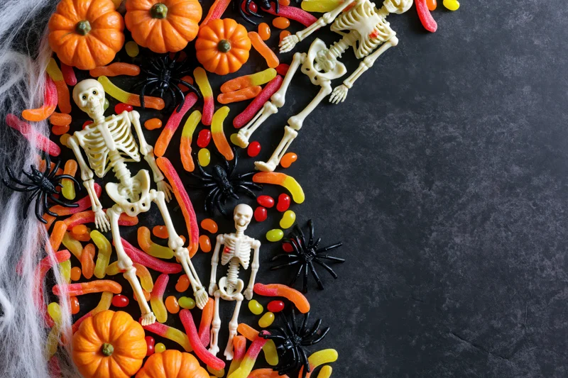 Plastic skeleton figurines and candy arranged on dark surface for halloween decoration