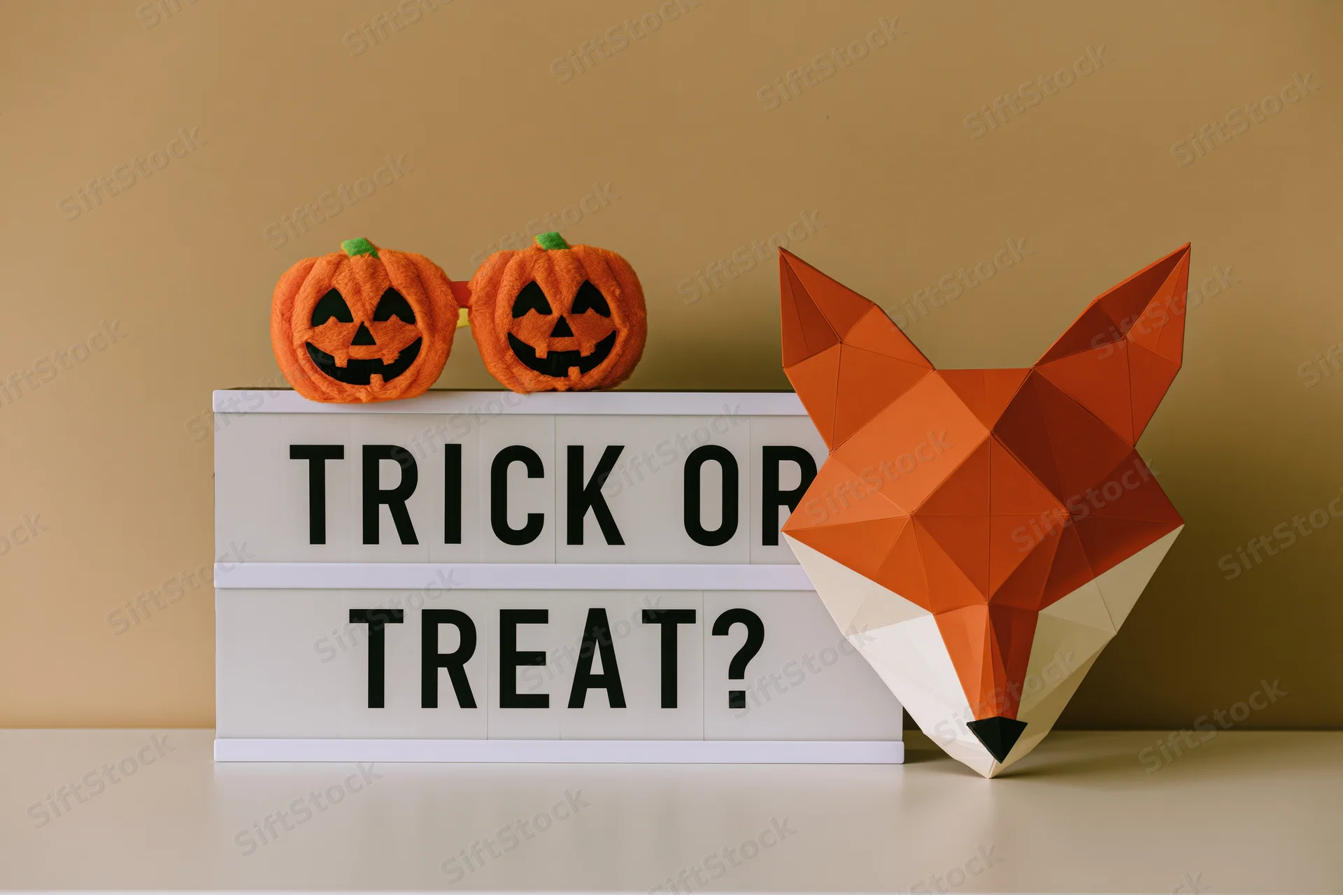 Lightbox sign reading trick or treat with orange pumpkins and geometric fox head on tabletop