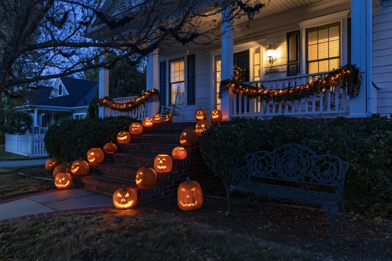 Carved jack-o-lanterns glowing on brick steps leading to a decorated house porch at twilight