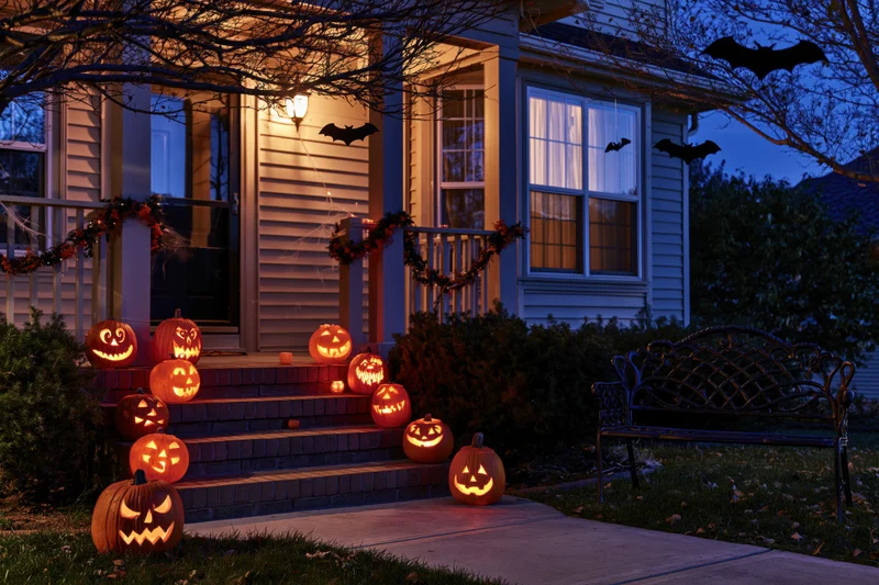 Carved jack-o-lanterns glowing on steps of a decorated house porch at night