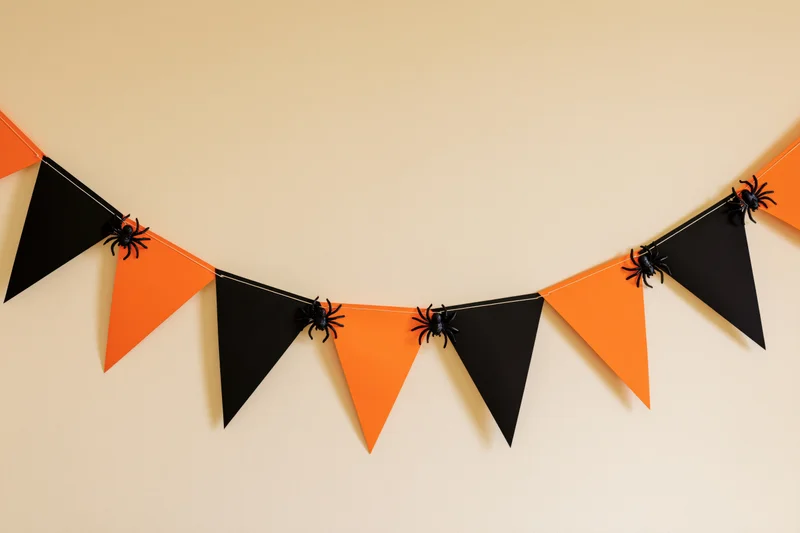 Orange and black triangular paper bunting with plastic spiders hanging on a wall for halloween decoration